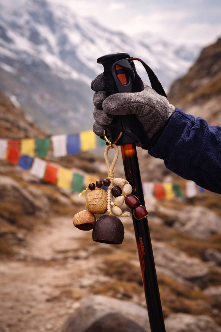 Hand holding a hiking pole with prayer flags and stones in the background